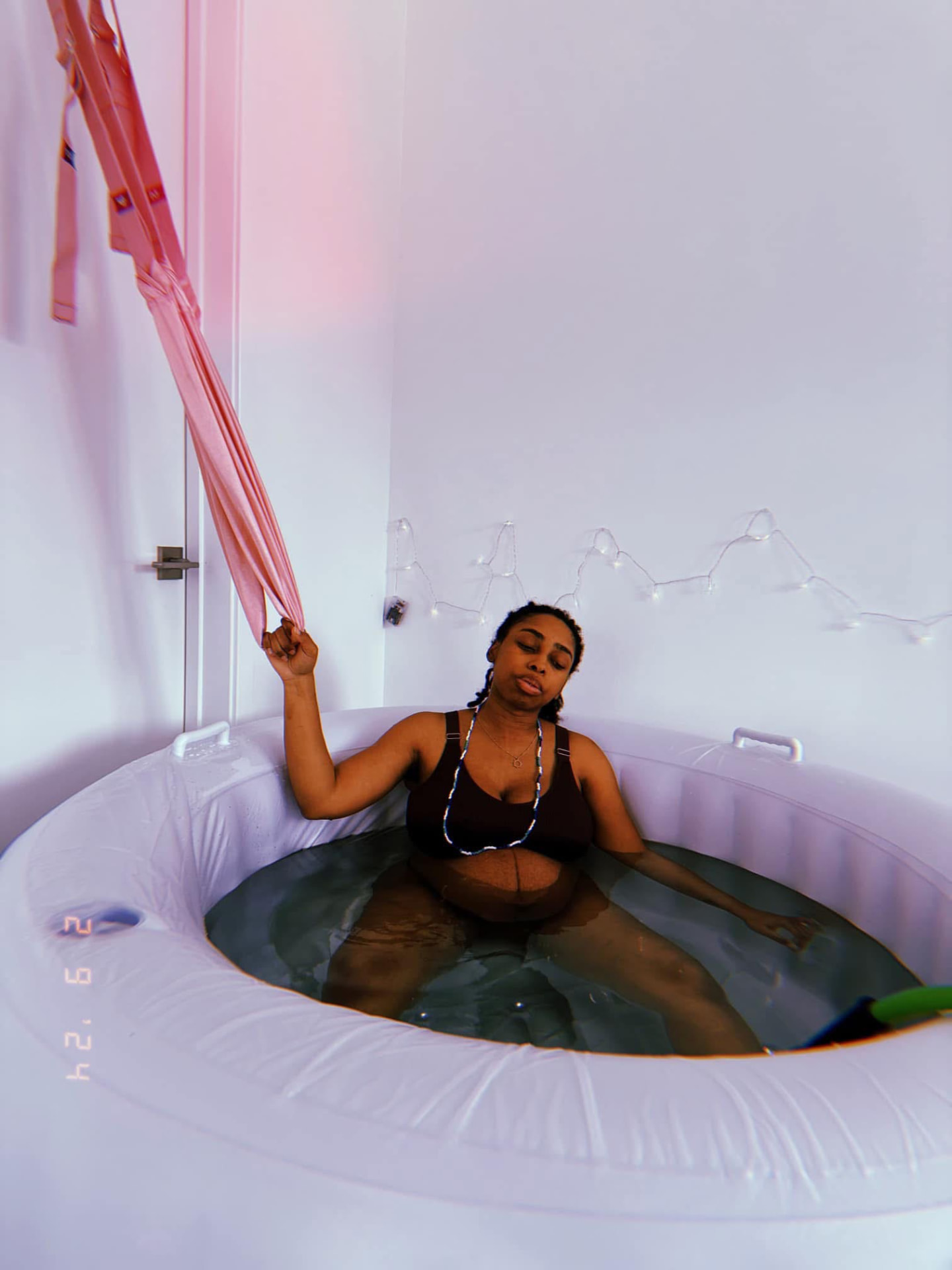 Mother laboring in a white inflatable birth pool at home, resting back with eyes closed