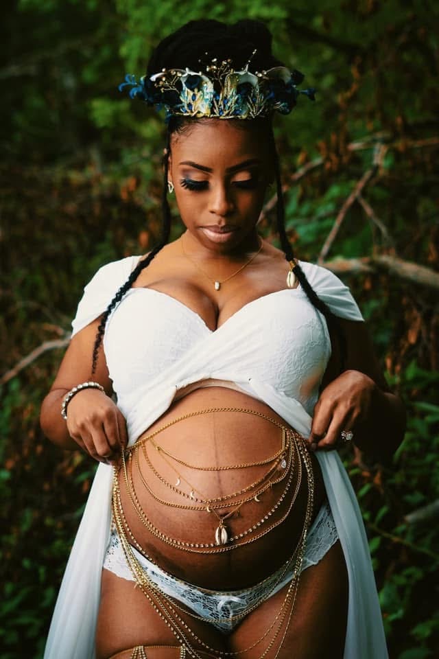 Expectant mother holding her gown open to reveal her belly draped in gold chains and cowrie shells
